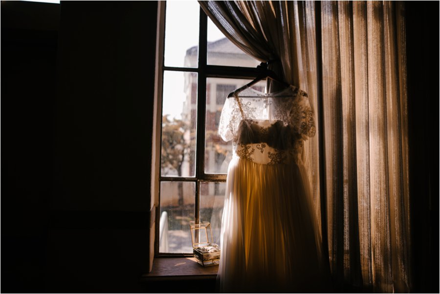 Moody wedding photo of dress hanging in window