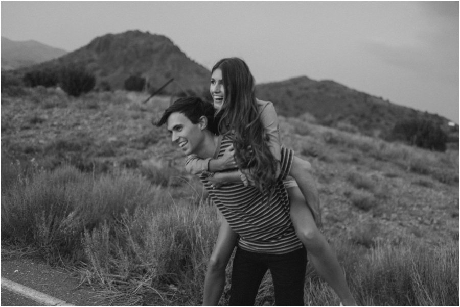 Guy giving his girlfriend a piggyback ride on their roadtrip through the desert.