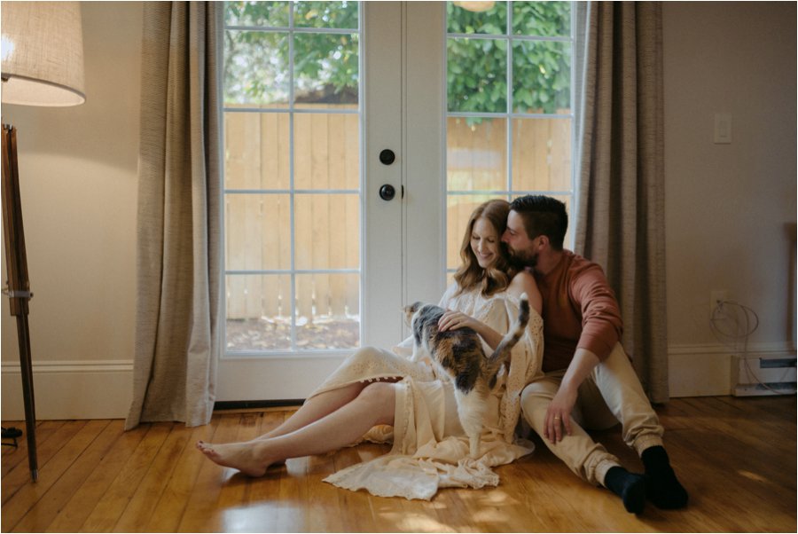 Couple cutting on the wood floor with their cat.  Girl wearing Fillyboo maternity dress.