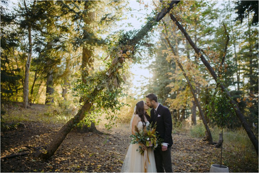 Bride & Groom first kiss under their floral rustic archway in Millcreek Canyon